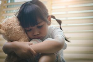 Close up lonely little girl hugging toy, sitting at home alone, upset unhappy child